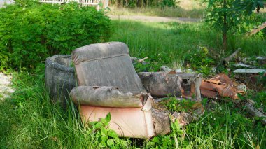 Eski, kırık bir koltuk, bir park ortamındaki çimlerin arasında uzanıyor. Döşeme yıpranmış ve renkleri solmuş. Koltuğun dolgusu ve iç yapısı ortaya çıkıyor. Sandalyenin etrafında enkaz ve yeşillik parçaları var..