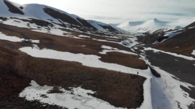 Svalbard (Spitsbergen) - insanlar yürüyüş yapıyor ve el sallıyor. Dağlar karla kaplı.