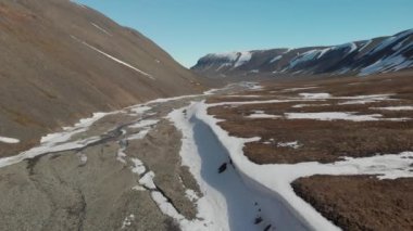 Svalbard 'da (Spitsbergen) güneşli bir gün, insanlar yürüyüş yapıyor. Güzel mavi gökyüzü ile buzulun aşağısında drone manzarası.