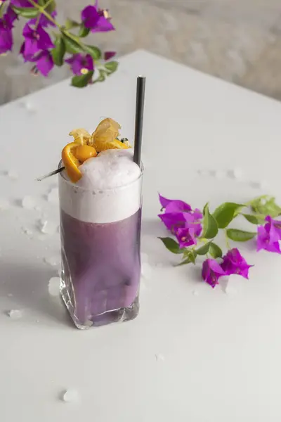 Purple Rain Glitter Cocktail on a white table decorated with a Gooseberry on the top