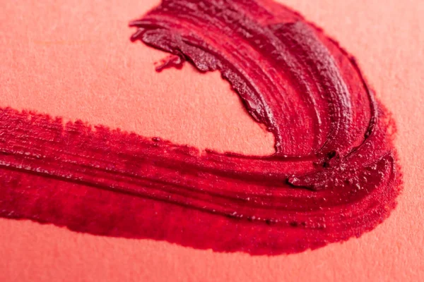 Brush strokes of red paint on peachy pink background, lipstick marks on paper