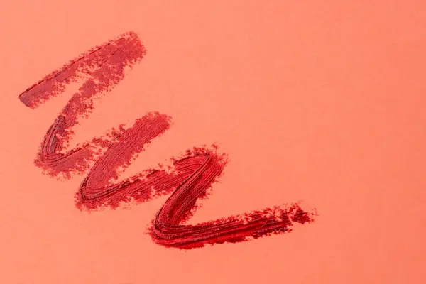 Brush strokes of red paint on peachy pink background, lipstick marks on paper