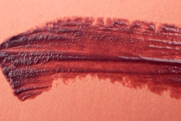 Brush strokes of red paint on peachy pink background, lipstick marks on paper