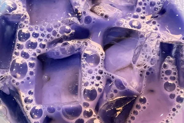 Colorful soapy liquid with bubbles closeup, cloudy water texture with transparent ice cubes and bubbles