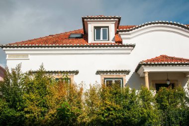 Kırmızı kiremit çatılı ve arka planda yeşil ağaçlı eski bir ev..