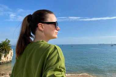 Denizin arka planında güneş gözlüklü genç bir kadının portresi