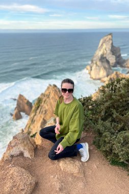 Portekiz 'deki Atlantik Okyanusu' ndaki uçurumların önünde meditasyon yapan genç bir kadın.