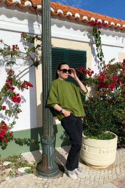 Yeşil tişörtlü ve kot pantolonlu genç bayan telefonda konuşuyor..