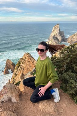 Portekiz 'de Atlantik Okyanusu kıyısında bir uçurumda oturan genç bir kadın..