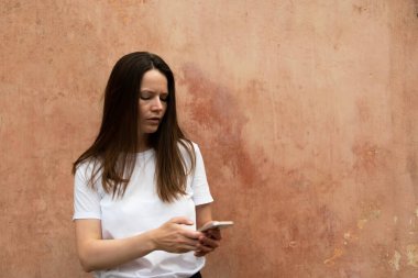 Genç bir kadın grunge duvarının önünde cep telefonuyla mesaj atıyor.