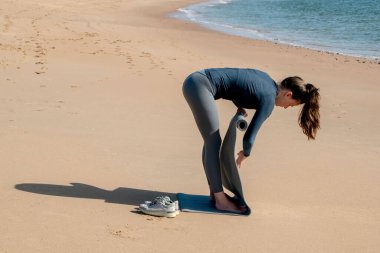 Plajda yoga minderinde şınav çeken genç bir kadın.