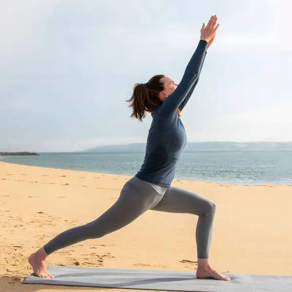 在海滨的垫子上练习瑜伽的年轻女子的全长肖像 — 图库照片