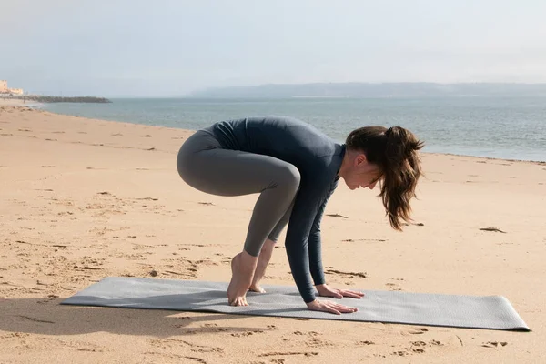 Sahilde yoga yapan genç ve çekici bir kadın. Spor kıyafetleri giyiyor.