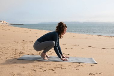 Genç çekici kadın sabahları sahilde yoga yapıyor.