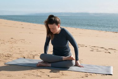 Kumsalda yoga yapan genç bir kadın. Sağlıklı yaşam tarzı ve rahatlama kavramı.
