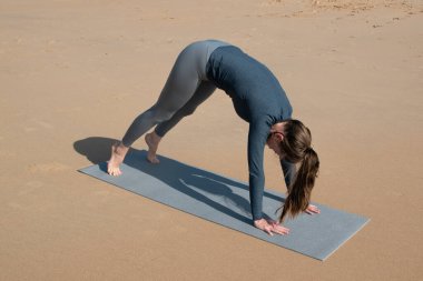 Genç bir kadın gündüz vakti plajda yoga yapıyor. Vücut ve zihinsel gelişim arasındaki sağlıklı yaşam tarzı ve doğal denge kavramı.