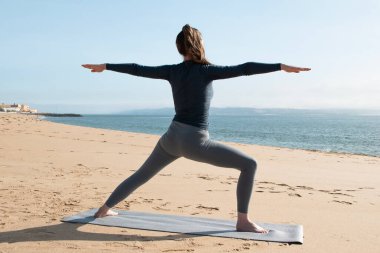Genç bir kadın güneşli bir günde sahilde yoga yapıyor.