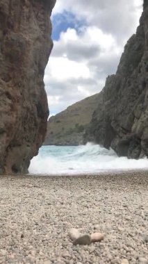 Büyük deniz dalgaları boş bir çakıl taşı plajında kayalara çarpar dramatik bir manzara, seyahat içeriği