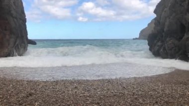 Büyük deniz dalgaları boş bir çakıl taşı plajında kayalara çarpar dramatik bir manzara, seyahat içeriği