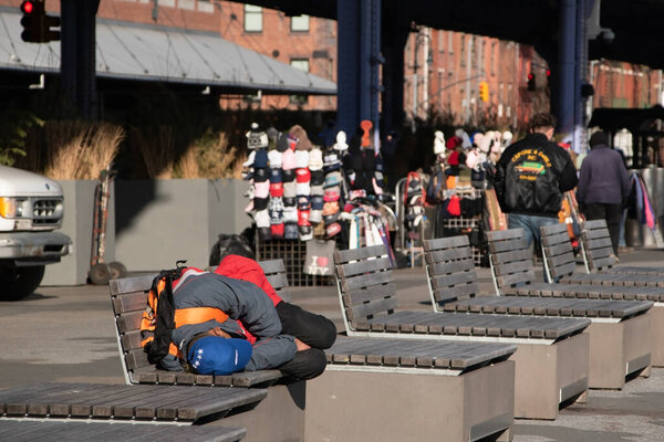 Бездомный спит на скамейке на рынке уличной еды в Нью-Йорке.
