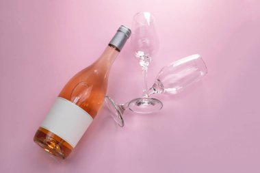 Bir şişe gül şarabı ve iki bardak pembe arka plan, üst manzara.