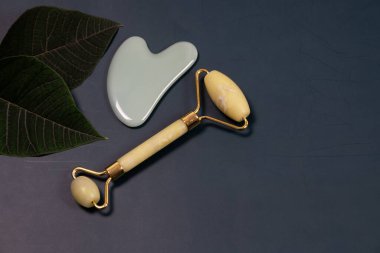 Yeşim yüz silindiri ve gri arkaplanda gua sha kazıyıcı