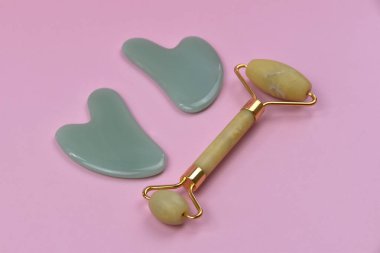 Yeşim yüz silindiri ve pembe arka planda gua sha taşları