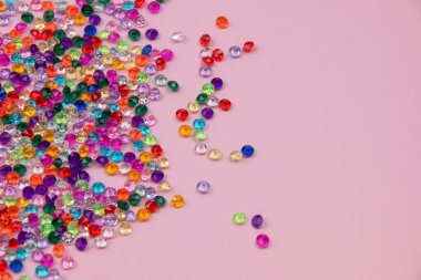 Renkli boncuklar pembe arka planda, üst manzarada, düz yerde serili.