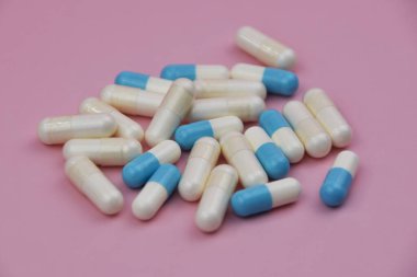 Pembe arka planda beyaz ve mavi kapsüller. Ön plana odaklan, yumuşak bokeh.