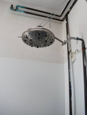 Duş başlığı duvarın önünde soyulmuş boya ve paslı borular.