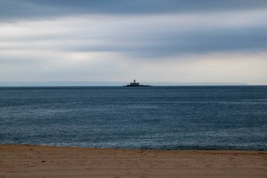 Denizin ortasında deniz feneri ve bulutlu gökyüzü olan bir deniz manzarası.