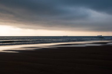 Günbatımı Normandiya, Fransa 'da sahilde, arkada bir gemi var.