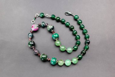 Gri arkaplanda doğal yeşil ve pembe boncuklardan yapılmış bilezik.