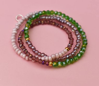 Pembe arkaplandaki çok renkli boncuklardan yapılmış bilezik.