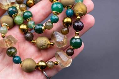 Elinde koyu arkaplanda yarı değerli taşlardan yapılmış bir bilezik var.