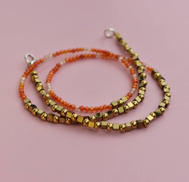 Pembe arka planda kırmızı ve turuncu boncuklardan yapılmış kolye.