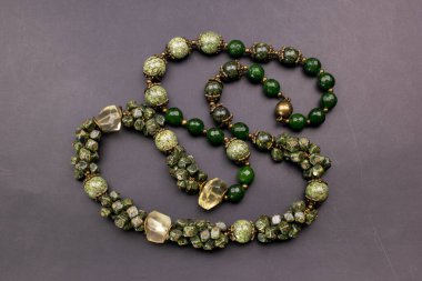 Gri arkaplanda doğal yeşil taşlardan yapılmış kolye..