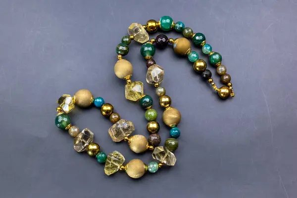 Gri zemin üzerinde yeşil taşlar olan kolye, üst görünüm