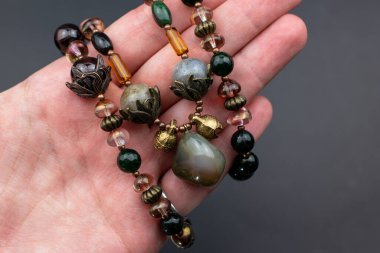 Karanlık bir arkaplanda doğal taşlardan bir kolye tutuyor.