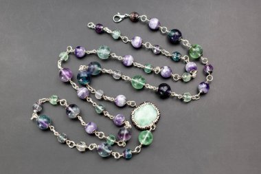 Gri arkaplanda yeşil zümrüt olan kolye..