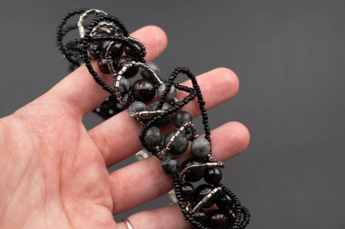 Gri arkaplanda siyah boncuklardan yapılmış bilezik.