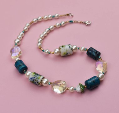 Pembe arka planda doğal taşlardan yapılmış kolye.