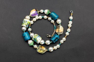 Siyah arkaplanda boncuklardan ve değerli taşlardan yapılmış bir kolye..