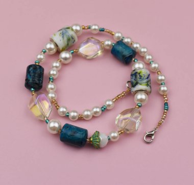 Pembe bir zemin üzerinde doğal taşlar ve boncuklardan yapılmış kolye.