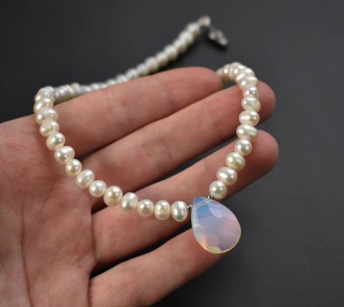 Avucunun içinde siyah bir arka planda inci kolye.