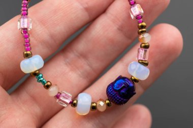 Karanlık bir arkaplanda değerli taşları olan bir bileziği tutan el.