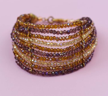 Pembe arka planda değerli taşlardan yapılmış bilezik.