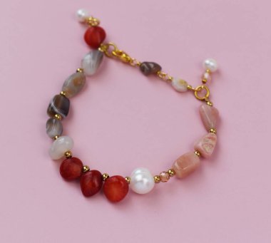 Pembe arka planda doğal değerli taşlardan yapılmış bir kolye..