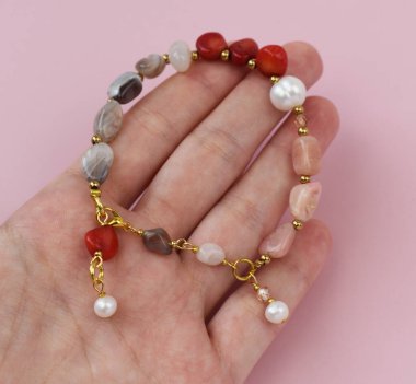 Pembe arka planda doğal taşlardan yapılmış bir bilezik..