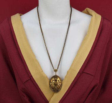 Kırmızı arka planda kırmızı ceketli bir mankenin üzerinde altın bir kolye.